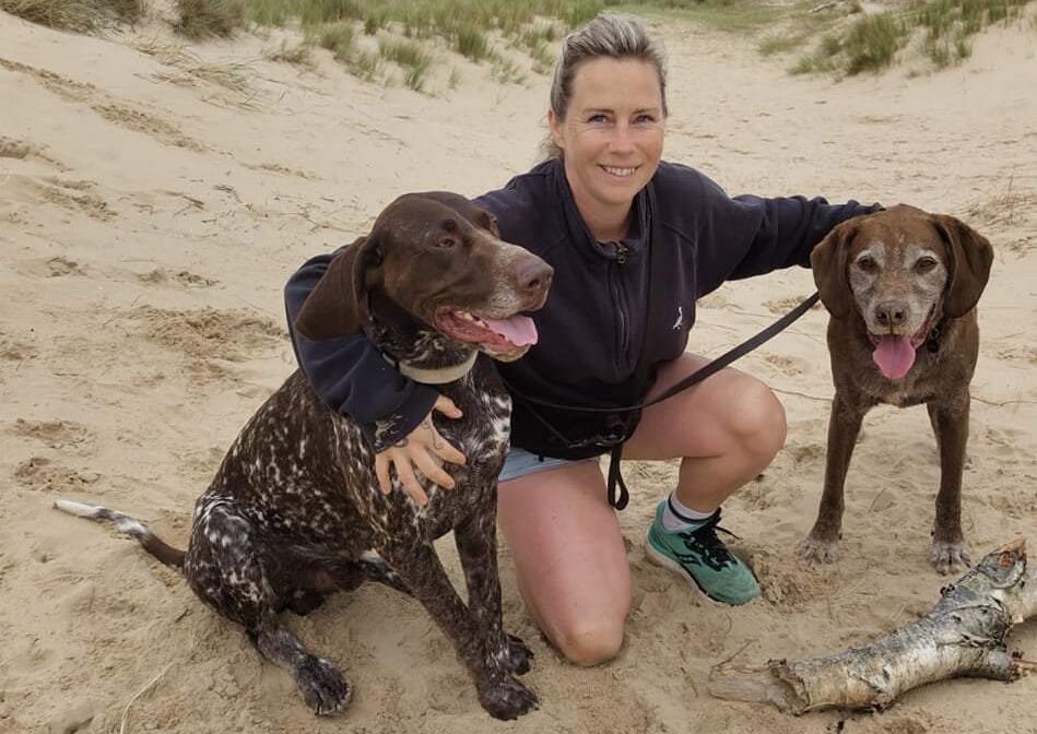 a woman kneeling with two dogs on a beach