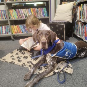 a girl sitting on a blanket with a dog in a library